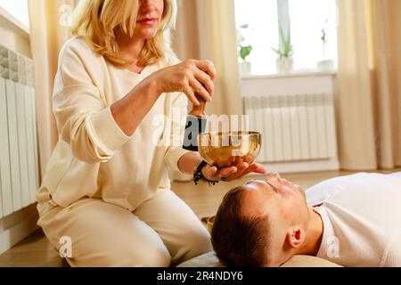 Woman playing on a tibetian singing bowl maling massage meditation for a man Stock Photo