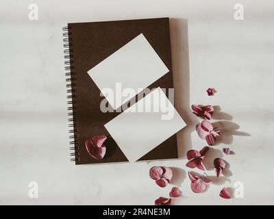 Two blank white cards, dry pink flowers on black notebook on white background with shadows top view. Forms for business, advertising. Empty space for Stock Photo