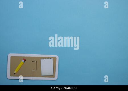 Picture puzzles placed on the edge of the blue background. Pen and notepad. Stock Photo