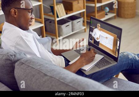 African American student sitting on couch with laptop and having online class via video call Stock Photo
