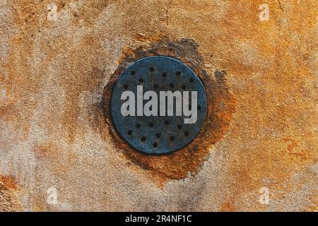 Worn round ventilation duct grille with holes on weathered house wall Stock Photo