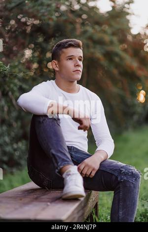 Teenager sitting on a park bench, looking away. Stock Photo