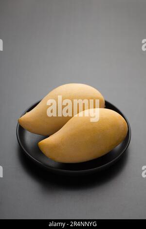 Ripe mangoes of Nam Dok Mai species of Thailand in a black wooden bowl. Stock Photo