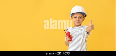 Little African-American electrician with tools showing thumb-up gesture on yellow background with space for text Stock Photo