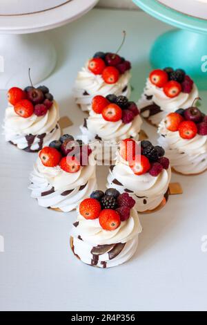 Delicious mini Pavlova meringue cakes decorated with fresh raspberry, strawberry and blueberry on white background Stock Photo