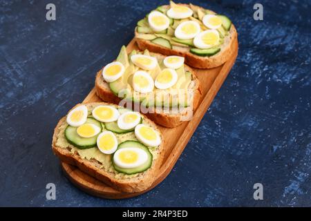 Tasty toasts with quail eggs, avocado and cucumber on dark blue background Stock Photo