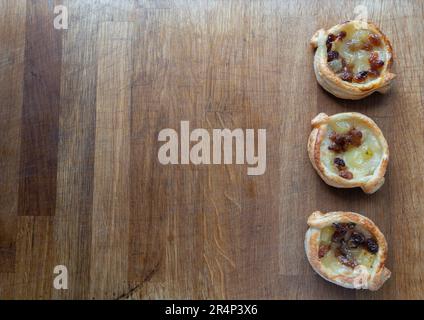 Indulge in the irresistible flavors of these Danish puff pastries, generously filled with apple and sultanas, showcased on a charming wooden chopping Stock Photo