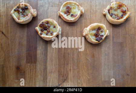 Prepare to be enchanted by these delectable Danish puff pastries, brimming with the sweetness of apple and sultanas, elegantly presented on a wooden c Stock Photo