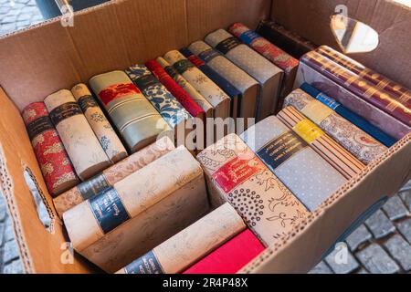 Box full of old used books, flea market. Vintage books with decorated fabric cover at street market. Stock Photo