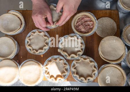 Discover the art of crafting a delicious Pork Pie: Expert hands skillfully crimping the pastry on a metal table, showcasing the culinary craftsmanship Stock Photo