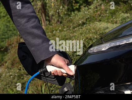 Person charging a black electric car with blue cable Stock Photo