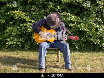 Man playing guitar in the park with face obscured by hat Stock Photo
