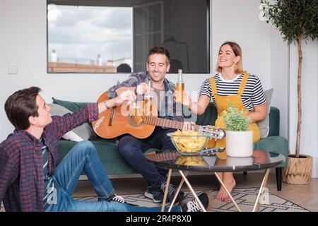 Group of friends having some beers and playing the guitar together at home. Concept: lifestyle, music, friendship Stock Photo