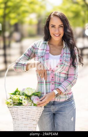 Beautiful young woman holding a basket with flowers during a sunny day. Stock Photo