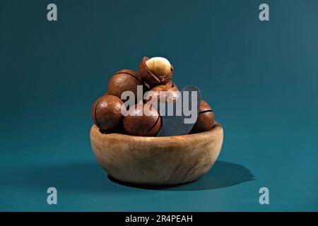 Macadamia nuts with a key in wooden bowl on a turquoise background Stock Photo