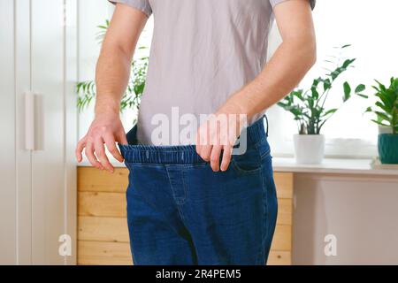 The guy is trying on big jeans after losing weight. Man in oversized pants in weight loss concept Stock Photo