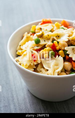 Pasta salad with bow-tie pasta, carrots, peas, corn, bell pepper, beans, chickpeas, olives and pickles. Stock Photo