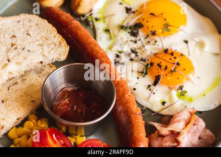 Fried eggs with sausages, tomato and bread on plate. English breakfast in cafe. European breakfast table. Eggs with meat and vegetables. Stock Photo