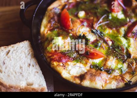 Fried eggs with tomato and ham in pan. Served breakfast table. Omelette with tomato and bread. Spanish tortilla. Eggs with pesto and vegetables. Stock Photo