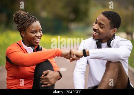Good workout outdoor. Glad young black couple relax, hitting fists, celebrate great result in summer, close up Stock Photo