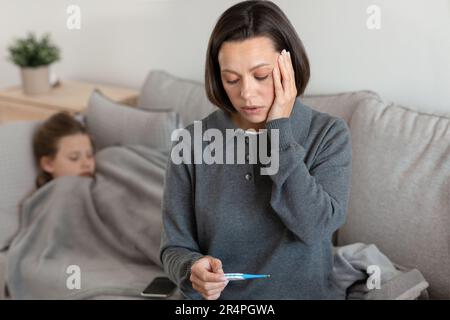 Worried unhappy caucasian mature mom looks at thermometer with high temperature Stock Photo