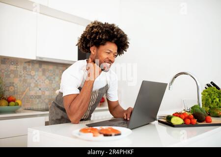 Chef Preparing Dinner Using Laptop For Recipes Search At Kitchen Stock Photo