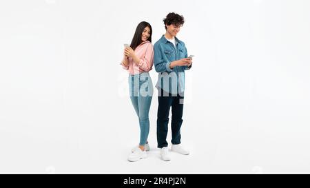 Young Couple Using Mobile Phones Texting Standing On White Background Stock Photo