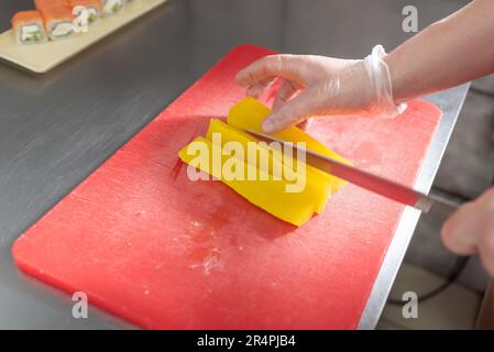 The cook cuts pickled daikon for sushi on a red board. High quality photo Stock Photo