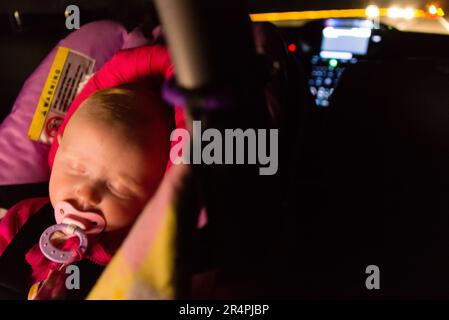 Five-month-old baby asleep in a car seat during a night drive. Stock Photo