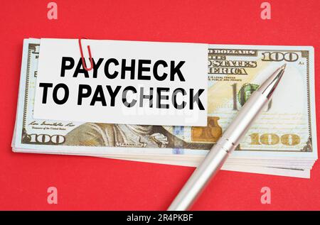 Business concept. On a red surface are dollars on which a pen and paper with the inscription - paycheck to paycheck Stock Photo