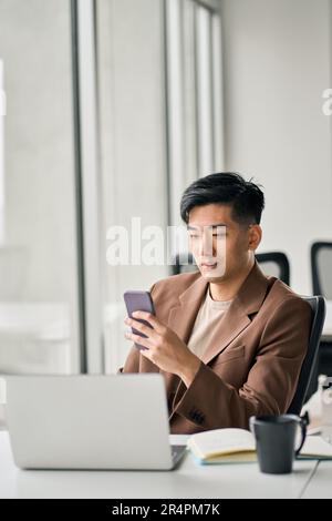 Young busy smiling Asian business man using mobile phone in office. Stock Photo