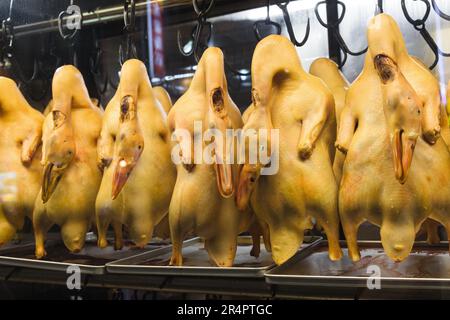 Roasted ducks hanging from metal meat hooks in the window of a