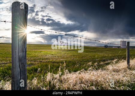 Prairie landscape scene with barbed wire fence overlooking a distant oil pump jack under a stormy sky in Rocky View County Alberta Canada. Stock Photo