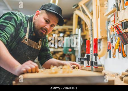 focused male carpenter blowing dust off a piece of wood and smiling to the camera, woodworking concept. High quality photo Stock Photo