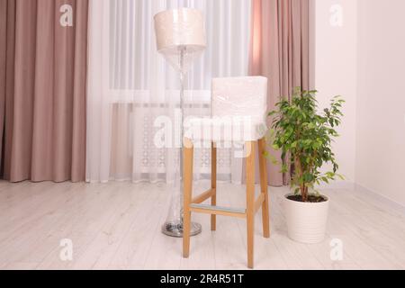 Lamp and chair wrapped in stretch film and houseplant indoors Stock Photo