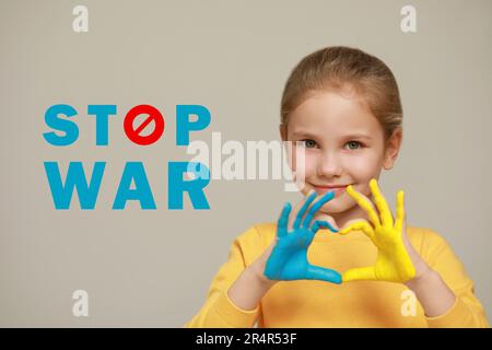 Stop war. Little girl making heart with her hands painted in colors of Ukrainian flag on light background Stock Photo