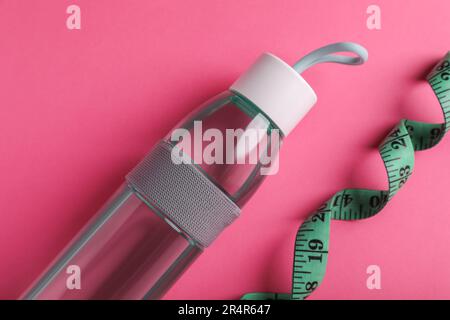 Measuring tape and bottle of water on pink background, flat lay. Weight control concept Stock Photo