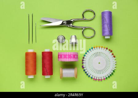 Flat lay composition with thimbles and different sewing tools on green background Stock Photo