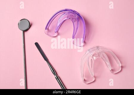 Bite correction. Transparent mouth guards and dentist tools on light pink background, flat lay Stock Photo