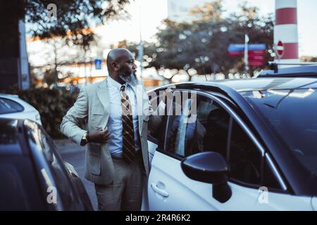 In the streets of Lisbon, a confident black man with a bald head and a long beard adjust his cream suit jacket with precision. Standing beside his whi Stock Photo
