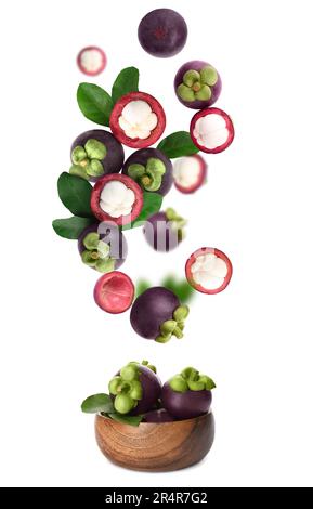 Many ripe mangosteen fruits and leaves falling into wooden bowl on white background Stock Photo