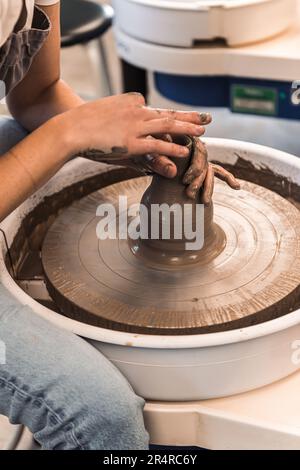 Young woman working on a pottery wheel shaping the brown clay with both hands Stock Photo