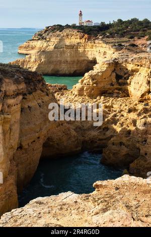 Carvoeiro, Portugal - December 25, 2019: Limestone cliffs in the Atlantic Ocean with Farol De Alfanzina Lighthouse in the distance on a sunny winter d Stock Photo