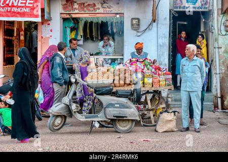 Mandawa, Rajasthan, India - Nov 17, 2015. People's daily lives on a neighborhood street with a snack food vendor's cart, scooter and laundry shop. Stock Photo