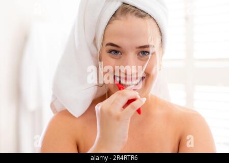 Closeup portrait of plus size smiling caucasian woman wrapped in towels brushing teeth in bathroom Stock Photo