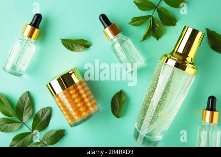 Cosmetic bottle containers with green leaves on mint background. Natural beauty product concept. Top view Stock Photo