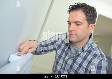 man regulates temperature in control panel of central heating Stock Photo