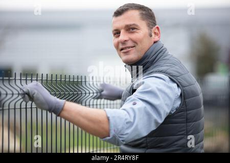 worker installing welded metal mesh fence Stock Photo