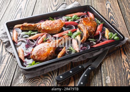 Homemade baked pork chops with red onions, herbs and rhubarb close-up in a baking sheet on the table. Horizontal Stock Photo