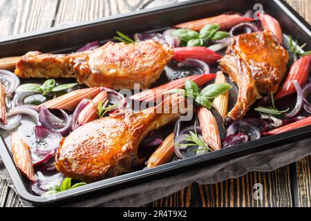 Baked pork chops with red onions, herbs and rhubarb in honey glaze close-up in a baking sheet on the table. Horizontal Stock Photo